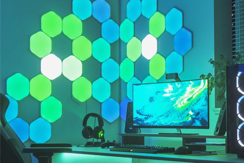 Nanoleaf Shapes Hexagon LED lights shining green in next to a computer on a wall. 